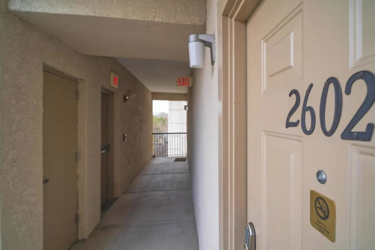 This image shows the entrance to a unit, with a clearly marked door number, an exit sign, and a well-lit hallway. The neutral decor suggests a welcoming and secure environment for guests coming and going throughout their stay.