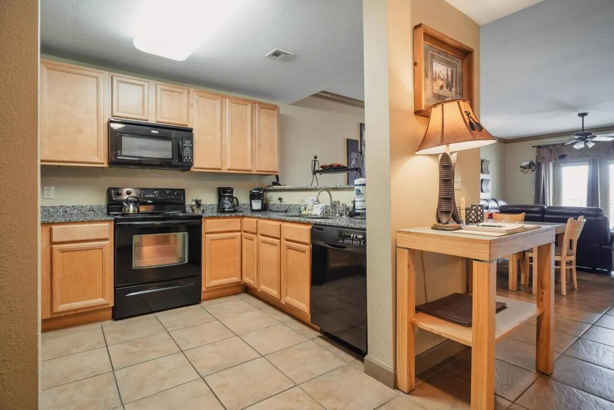 This image features a view of the kitchen appliances and countertops, as well as the adjacent dining area. Modern appliances are visible, including a stove, refrigerator, and microwave, along with stylish lighting fixtures and tasteful decorative elements. The open layout allows a seamless flow between the kitchen and dining space, capturing the inviting ambiance of the heart of the condo.