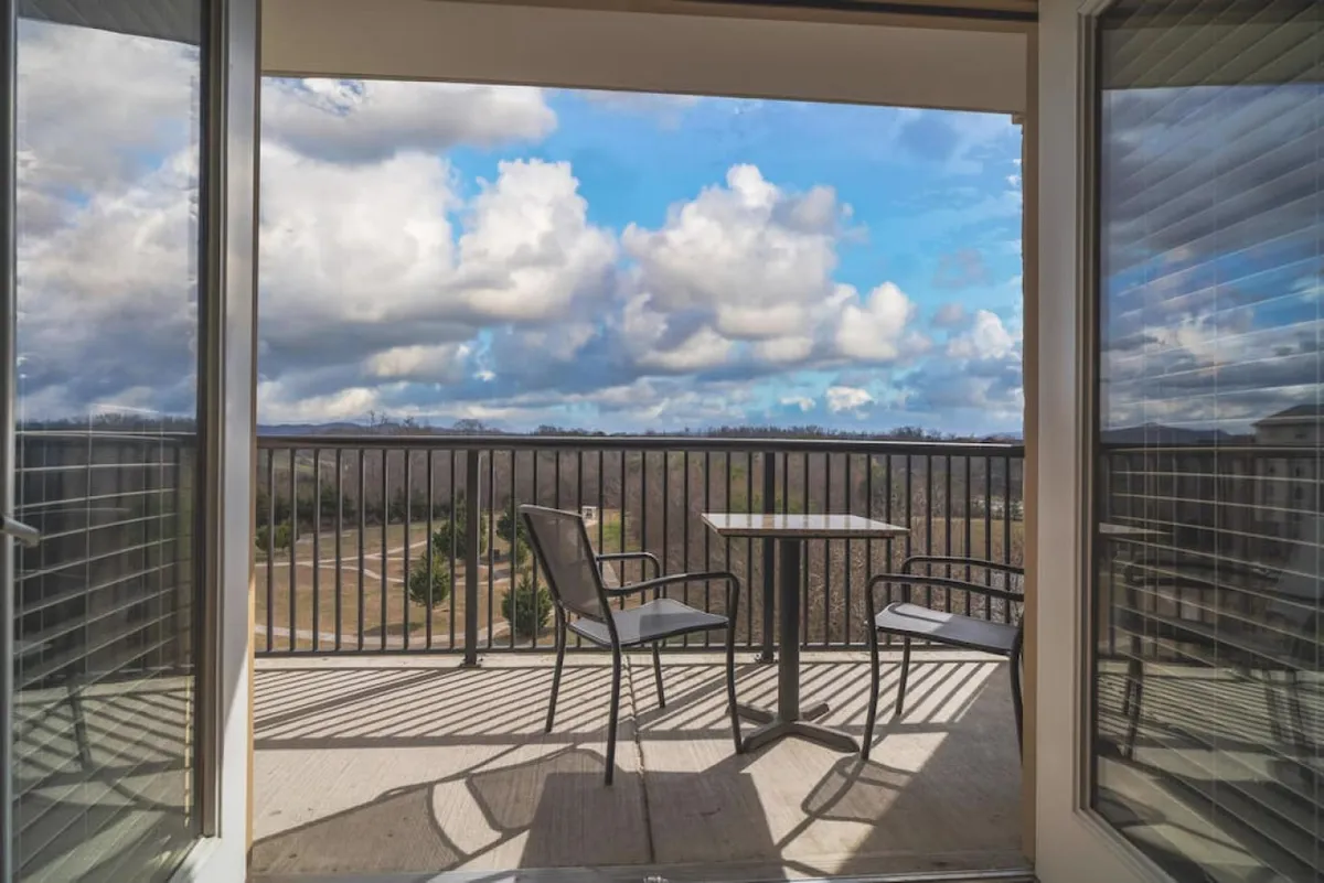 A private balcony with a table and comfortable chairs overlooks the scenic Smoky Mountains. The setting is tranquil, perfect for morning coffee or relaxing with a book. The natural landscape and the elevation of the balcony suggest both privacy and connection to the outdoors.