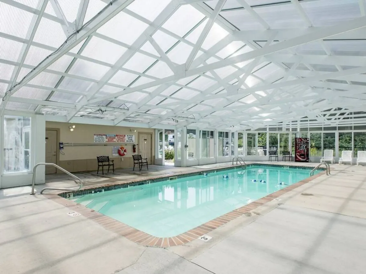 An inviting indoor swimming pool with a white lattice structure overhead, a spacious seating area, and ample natural light. The pool is heated and accessible year-round, offering a relaxing oasis for guests regardless of the season.