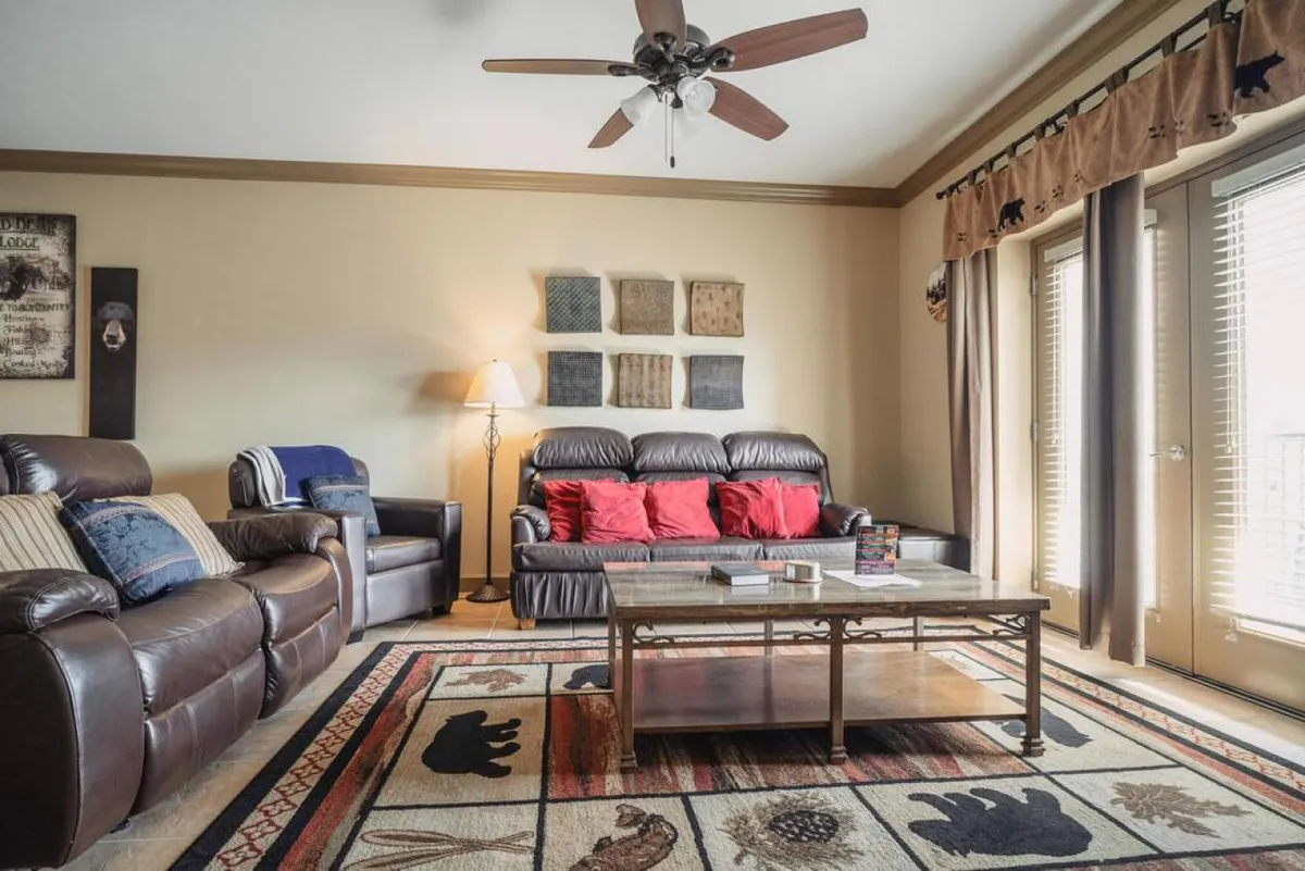 A cozy living area with leather couches, a bear-motif rug, and a central coffee table. The inviting mood is perfect for socializing, reading, or game nights, and the decor hints at a mountain getaway vibe.