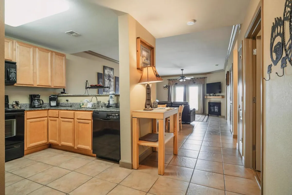 This image showcases the kitchen cabinetry, a spacious dining table, and a portion of the living room seating, all arranged in a harmonious open-concept layout. The inviting table is set for dining, emphasizing the communal aspect of the space, while the visible cabinetry hints at ample storage for meal prep essentials.